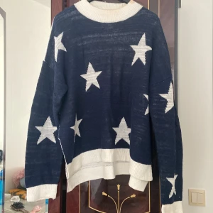 Mörkblå stickad tröja med stjärnor från Tommy Jeans - Säljer en mörkblå stickad tröja från Tommy Jeans med vita stjärnor. Tröjan har långa ärmar och vita ribbade muddar vid ärmslut och nederkant. Använd 2 gånger