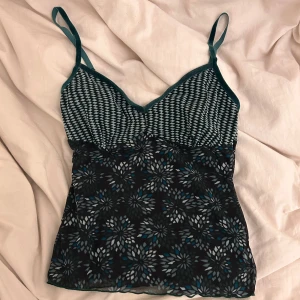 Mönstrad linnetopp med justerbara axelband - Snygg linnetopp med blommigt mönster i svart, blått och grått. Toppen har justerbara axelband och en v-ringad design. Perfekt för en stilren look. Kawaii osv 