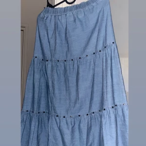 Blå långkjol med volanger - Snygg blå långkjol med volanger och elastisk midja. Perfekt för en avslappnad stil. Kjolen har dekorativa detaljer som ger en extra touch.