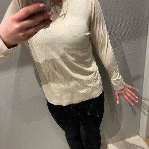 Beige långärmad tröja - Säljer en stilren beige långärmad tröja i mjukt material. Perfekt för en avslappnad look. Tröjan har en enkel design med rund hals och är lätt att matcha med olika outfits. Små slitningar i fram men inget man lägger märke till