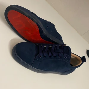Mörkblå sneakers med röd sula - Snygga mörkblå sneakers från Christian Louboutin med en iögonfallande röd sula. Skorna har snörning och är tillverkade i mocka, vilket ger en lyxig känsla. Perfekta för dig som vill ha en stilren men ändå unik look. Har tappat bort box och kvitto därför pga av priset. Passar 40/41