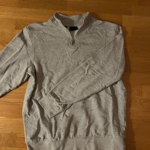 Grå tröja med dragkedja från bpc - Säljer en stilren grå tröja från bpc med halv dragkedja och långärmad design. Perfekt för en avslappnad look. Tröjan har en mjuk insida som håller dig varm under kyliga dagar.