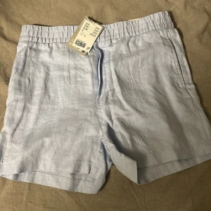 Ljusblå linne shorts från H&M - Säljer ett par ljusblå shorts från H&M i linne. De har en elastisk midja och två bakfickor. Oanvända med prislapp kvar