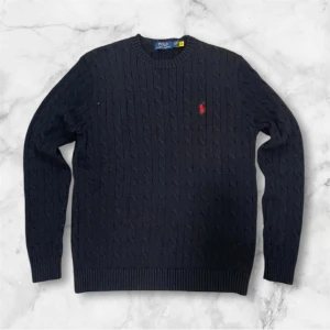 Svart stickad tröja från Polo Ralph Lauren - Säljer en stilren svart stickad tröja från Polo Ralph Lauren med kabelstickat mönster. Tröjan har långa ärmar och ribbstickade muddar vid ärmslut och nederkant. Storlek S och bra skick!