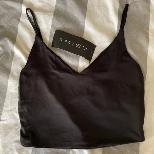 Svart linnetopp från Amisu - Snygg svart linnetopp från Amisu NEW YORKER med smala axelband och v-ringning. Perfekt för en stilren look. Tillverkad i ett mjukt och glansigt material.