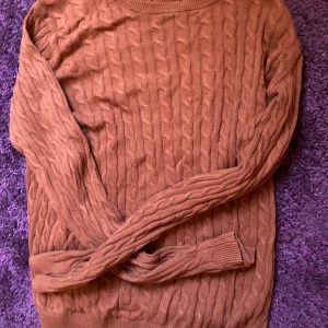 Röd-Brun kabelstickad tröja “Basic You” - Säljer en röd-brun kabelstickad tröja från Basic You med rund hals och långa ärmar. Tröjan har ett klassiskt flätmönster och ribbade muddar vid hals, ärmslut och nederkant. Storlek sak as men passar S/M.