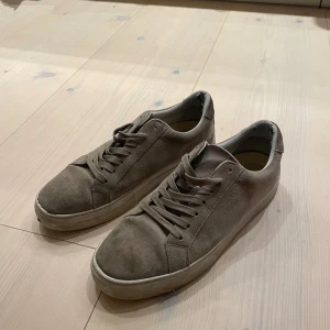 Beige mockasneakers från J.Lindeberg - Snygga sneakers i beige mocka från J.Lindeberg med klassisk låg profil och rund tå. Skorna har matchande snörning och en vit platt sula som ger en clean look. Perfekta för dig som gillar stilrena och minimalistiska skor.
