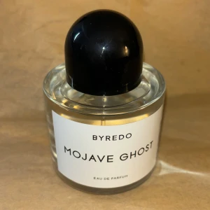 Byredo Mojave Ghost Eau de Parfum - Byredo Mojave Ghost Eau de Parfum i en stilren, rund glasflaska med vit etikett och svart blank kupolformad kork. Parfymen har en transparent vätska och flaskan känns lyxig och minimalistisk, perfekt för dig som gillar exklusiva dofter. Låda finns. 
