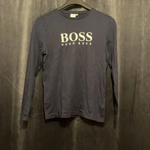 Mörkblå långärmad tröja Hugo Boss - Snygg mörkblå långärmad tröja från Hugo Boss med vit logga framtill. Tröjan är i mjuk bomull med en klassisk passform och rund halsringning. Perfekt för dig som gillar stilrena och enkla plagg med premiumkänsla.