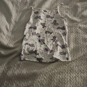 Pjamas linne med unicorn  - Supersöt vit linne-topp från H&M med gulligt enhörningsmönster och små regnbågar. Tunt axelbandslinne i mjuk bomull, perfekt för varma dagar eller som ett lager under andra plagg. Passar dig som gillar lekfulla och färgglada prints!