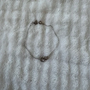Silverfärgat armband med ringar - Snyggt och stilrent armband i silverfärg med två sammanlänkade ringar i mitten. Ena ringen har små stenar som ger extra bling, medan den andra är slät. Perfekt för dig som gillar minimalistiska smycken med en twist.