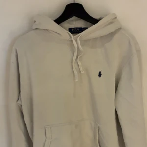 Vit hoodie från Polo Ralph Lauren - Säljer en klassisk vit hoodie från Polo Ralph Lauren med broderad marinblå logga på bröstet. Tröjan har huva med snörning och en stor magficka. Perfekt för en chill och stilren look. Finns fläckar som man ser på bilden men de går bort med pink stuff