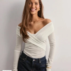 Vit omlott offshoulder topp - Snygg vit omlottopp med offshoulder-design och långa ärmar. Toppen har en figurnära passform och markerad midja med omlottdetalj framtill. Perfekt för dig som gillar stilrena och trendiga plagg. Helt ny aldrig använd, prislappen är kvar. Pris går och diskutera💕