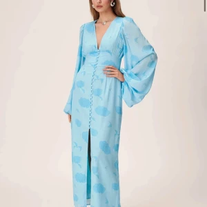 Adoore Positano Dress - En så fin klänning från ADOORE. En ljusblå lång klänning med fint mönster och knappar framtill. Stängs med dragkedja baktill. Säljer pågrund av fel storlek! Klänningen säljs inte längre hos adoore så passa på! Endast använd två gånger och har inga tecken på användning. Säljs för 1100💕PRIS KAN DISKUTERAS!  (Nypris 1695kr) 