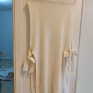 Vit långklänning med knyt i sidan - Säljer en stilren vit långklänning med snygga knytband i sidorna. Klänningen har en rak och enkel design utan ärmar, vilket ger en clean och modern look. Perfekt för dig som gillar minimalistisk stil och vill ha något som sticker ut med detaljerna på sidorna.