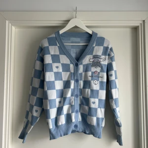 Blåvit rutig kofta med Cinnamoroll - Supergullig blåvit kofta med rutigt mönster och små hjärtan. Broderad Cinnamoroll-figur och texten 'Happy days together' på framsidan. Långärmad med ribbade muddar och knappar framtill. Perfekt för dig som gillar kawaii-stil och mjuka material. 