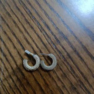 Guldiga chunky örhängen - Säljer ett par chunky örhängen i guld med snyggt texturerad yta. De är halvcirkelformade och har en cool, modern vibe som lyfter vilken outfit som helst. Perfekta för dig som gillar statement-smycken och vill sticka ut lite extra.