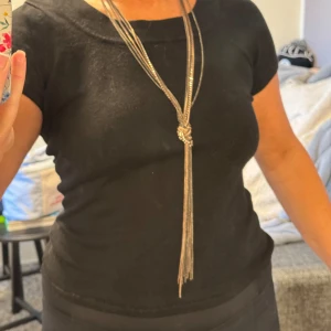 Långt silverfärgat halsband med knut - Säljer ett långt halsband i silverfärgad metall med flera tunna kedjor som samlas i en snygg knut framtill. Halsbandet har en glittrig känsla och hänger ner med fransar, perfekt för att ge din outfit lite extra edge.