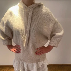 Beige stickad hoodie med snören - Mysig beige stickad hoodie med breda ärmar och ribbade muddar. Tröjan har huva och snörning framtill, perfekt för lager-på-lager och chill vibes. Oversized passform som ger en avslappnad look. Lite nopprig men inget märkvärdigt! 🩷🩷🩷🫶🏼