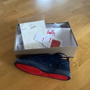 Mörkblå sneakers från Louboutin - !!Priset kan diskuteras vid snabbaffär!!Snygga mörkblå sneakers från Louboutin i mocka med klassisk röd sula och broderad logga på hälen. Skorna har rund tå, platt sula och snörning. Insidan är fodrad i beige läder för extra komfort. Perfekta för dig som vill sticka ut med exklusiv stil. 