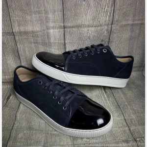 Mörkblå lanvin sneakers med lackad tå - Snygga mörkblå sneakers med vit sula och cool lackad tå. Skorna har snörning och är gjorda i mocka med en glansig detalj framtill. Perfekta för dig som vill ha en stilren men ändå unik look.