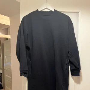 Svart oversized sweatshirt med fickor - En svart oversized sweatshirt med långa ärmar och praktiska sidofickor. Tröjan har en klassisk rund halsringning och är gjord i mjuk bomullsmix som känns skön mot huden. Perfekt för en chill och avslappnad stil.