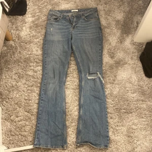 Blå bootcut jeans från Gina Tricot - Säljer ett par blå bootcut jeans från Perfect Jeans med snygg slitning på låret och knät. Jeansen har klassisk femficksdesign, normal passform och är tillverkade i jeansmaterial. 