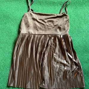 Brun plisserad top Gina Tricot - Snygg brun top från Gina Tricot i storlek L. Topen har smala axelband, plisserad, och ett band i midjan för extra detalj. Materialet är glansigt och ger en lyxig känsla. Perfekt för dig som gillar stilrena och trendiga plagg.