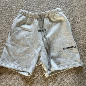 Grå Essentials shorts Fear of God - Snygga grå shorts från Fear of God Essentials med elastisk midja och långa snören framtill. Mjukt bomullsmaterial, fickor på sidorna och en bakficka. Perfekta för chill dagar eller streetwear-stil. Skriv för annan info. 
