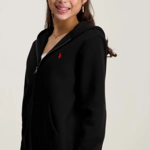 Svart hoodie från Polo Ralph Lauren - Svart hoodie från Polo Ralph Lauren med röd broderad logga på bröstet. Tröjan har huva, dragkedja framtill och praktiska fickor. Tillverkad i mjuk bomull som är skön att ha på sig. Perfekt för chill dagar och enkel att matcha med jeans eller joggers. Pris kan diskuteras men köpte den för 1300kr så kan inte gå mycket lägre än 700kr