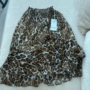 Leopardmönstrad kortkjol från Guess - Supersnygg kortkjol från Guess med leopardmönster och volangdetaljer. Kjolen har en bred, smockad midja och är gjord i ett lätt, transparent syntetmaterial som ger en cool och luftig känsla. Perfekt för dig som vill sticka ut med djurprint!