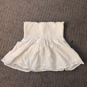 Vit bandeau tubtopp från Gina Tricot - Supersöt vit bandeau tubtopp från Gina Tricot med smockad överdel och volangig nederkant. Enkel att matcha med jeans eller kjol för en chill look.