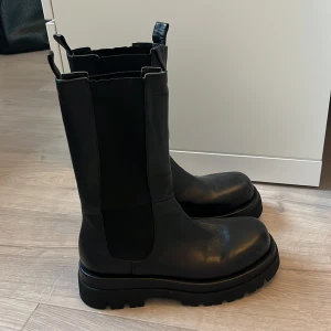  Svarta boots i skinn - Köpes för 1 500kr nypris på Nakd. Säljer ett par svarta chunky boots med högt skaft. Skorna är i skinn och har elastiska paneler på sidorna för enkel påtagning. Perfekta för dig som gillar en edgy och trendig look till höst och vinter.