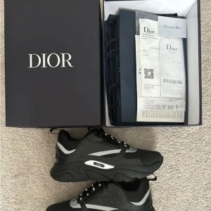 Svarta Dior sneakers med silvriga detaljer - Chunky svarta sneakers från Dior med silvriga detaljer och meshpaneler. Snygg design med rund tå, platt sula och snörning. Dior-logga på sidan. Perfekta för dig som gillar exklusiva och trendiga sneakers med sportig vibe. Äkta kvitto och alla storlekar finns !