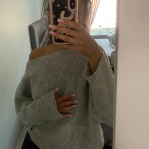 Grå offshoulder stickad tröja - Supermysig grå stickad tröja med offshoulder-design och lång ärm. Tröjan har en loose passform och är perfekt för dig som gillar en avslappnad och trendig stil. Passar perfekt till jeans eller leggings för en chill look.