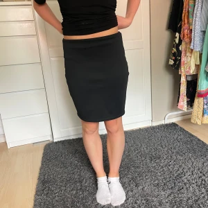 Svart tight kjol från NLY One - En stilren svart kjol från NLY One i storlek S. Kjolen är kort och har en tight passform som sitter snyggt runt kroppen. Enkel design utan detaljer eller mönster, perfekt för dig som gillar minimalistisk stil. Materialet känns mjukt och stretchigt.