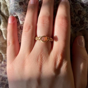 Guldfärgad wire ring med orange sten - Unik handgjord ring med guldfärgad wire och en oval, ”sunstone” i mitten. Ringen har snygga snurrade detaljer längs bandet som ger en cool boho-vibe. Perfekt för dig som gillar statement-smycken och vill sticka ut med något annorlunda.