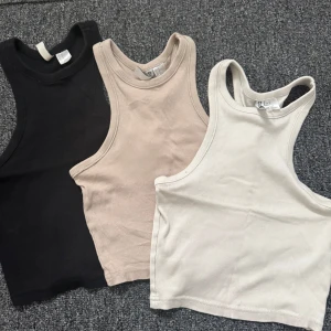 3-pack ribbade linnetoppar - Tre ribbade linnetoppar i svart, beige och vit. Modellen är croppad med breda axelband och rund halsringning. Perfekta att matcha med jeans eller kjol. Samtliga är i strlk XS men passar även S