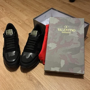 Valentino Rockrunners  - Säljer ett par svarta Valentino Garavani Rockrunner sneakers med kamouflagemönster. Skorna har snörning, rund tå och är tillverkade i en mix av skinn och syntet. Kommer med originalkartong och röd dustbag. Säljer dessa då det inte var min storlek, HELT nya