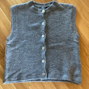 Grå stickad väst med knappar - Mysig grå stickad väst från Gina Tricot med rund halsringning och knäppning framtill. Jättefin att bära över en skjorta eller annan topp. Aldrig använd. 