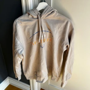 Beige hoodie från H&M - Säljer en beige hoodie från Hk&M med tryck framtill i orange och blått. Tröjan har huva med dragsko och långa ärmar. Perfekt för en avslappnad och stilren look.