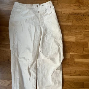 Skitcoola vita nylonbyxor DSWT från Japan - Säljer ett par vita byxor från Still By Hand, tillverkade i Japan. Inköpta på thisthingofours 2022. Byxorna har oversized passform, raka ben och stängs med knapp och dragkedja. Materialet är nylon vilket ger en lätt och modern känsla. Perfekta för dig som gillar stilrena och minimalistiska plagg.
