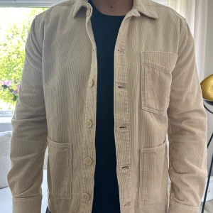 Beige manchester overshirt  - Säljer en beige overshirt i manchester från These glory days (skandinavia) Skjortan har tre stora fickor framtill och knäppning med matchande knappar. Perfekt att slänga över en t-shirt för en avslappnad look. Storlek M