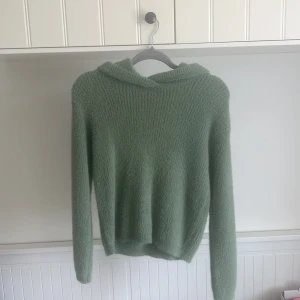 Grön fluffig hoodie - Mysig ljusgrön hoodie med luva och lång ärm. Tröjan är fluffig och mjuk, perfekt för kyliga dagar. Enkel och stilren design utan synliga detaljer eller mönster. Från Kappahl, knappast använd.