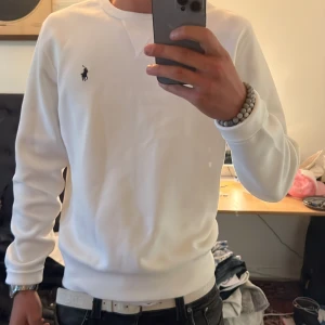Vit sweatshirt från Polo Ralph Lauren - Säljer en stilren vit sweatshirt från Polo Ralph Lauren med klassisk broderad logga på bröstet. Tröjan har rund halsringning och långa ärmar. Perfekt för en clean och enkel look.