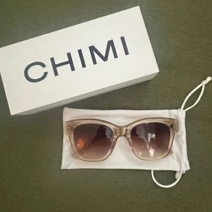 Chimi 07 Ecru - Modell 07 i Ecru. Stilrena solglasögon från CHIMI i en transparent beige färg med fyrkantig form. Snygga bruna tonade glas och diskret logga på skalmen. Kommer med vit förvaringspåse och box. En liten defekt och det är en liten rispa på sidan (se sista bilden), annars i nyskick!