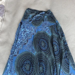 Blå långklänning med mandalamönster - Säljer en blå långklänning med snyggt mandalainspirerat mönster i olika blå nyanser. Klänningen har knyt i midjan och är ärmlös, perfekt för varma dagar. Materialet känns lätt och luftigt.