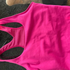 Rosa träningstopp från Stronger - Säljer en starkt rosa träningstopp från Stronger i storlek XS. Toppen har brottarrygg och är tillverkad av återvunnen polyester och elastan, vilket gör den stretchig och bekväm för träning. Skriv till mig för frågor😊🫶🩷