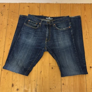 Blå jeansbyxor från Grant - Säljer ett par klassiska blå jeans från Grant med fem fickor och snygga slitningar. Byxorna har normal passform och raka ben. Märke och storlek syns tydligt på etiketten baktill. Perfekta för dig som gillar tidlös denimstil.