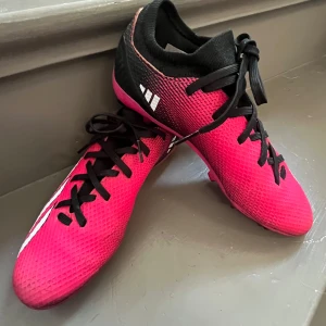 Rosa fotbollsskor från Adidas - Säljer ett par snygga rosa fotbollsskor från Adidas med svarta och vita detaljer. Skorna har snörning och en åtsittande passform med låg profil. Perfekta för dig som vill sticka ut på planen!Dom är lite svarta där fram men det är inget som syns på håll, fick dom ungifär för 1 år sen💞